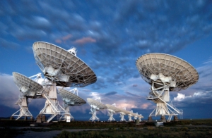 Photo of ten VLA antennas pointing at a cloudy sky at twilight.