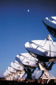 A photo of a line of VLA antennas underneath a partial moon.