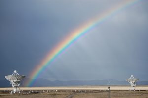 A photo of a rainbow over the VLA telescope in the desert.