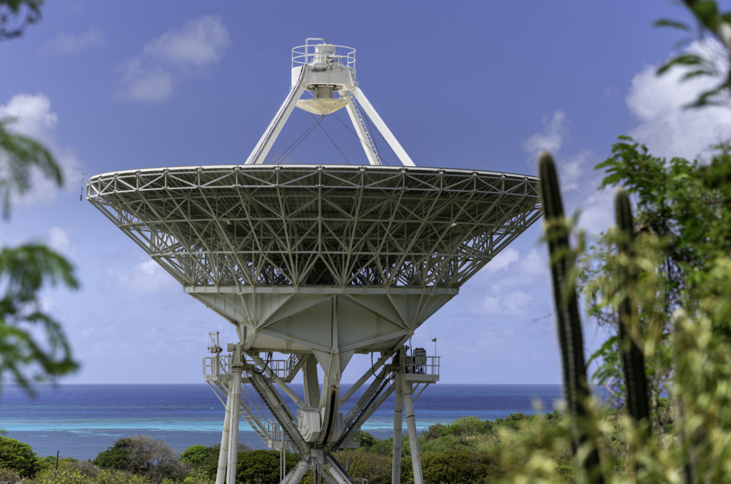 The St. Croix VLBA antenna is seen in front of the turquoise blue ocean that surrounds the island.