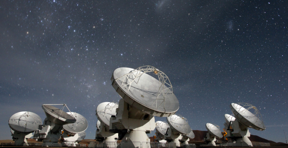 Photo of the moon-illuminated ALMA radio telescope array with stars in the background.